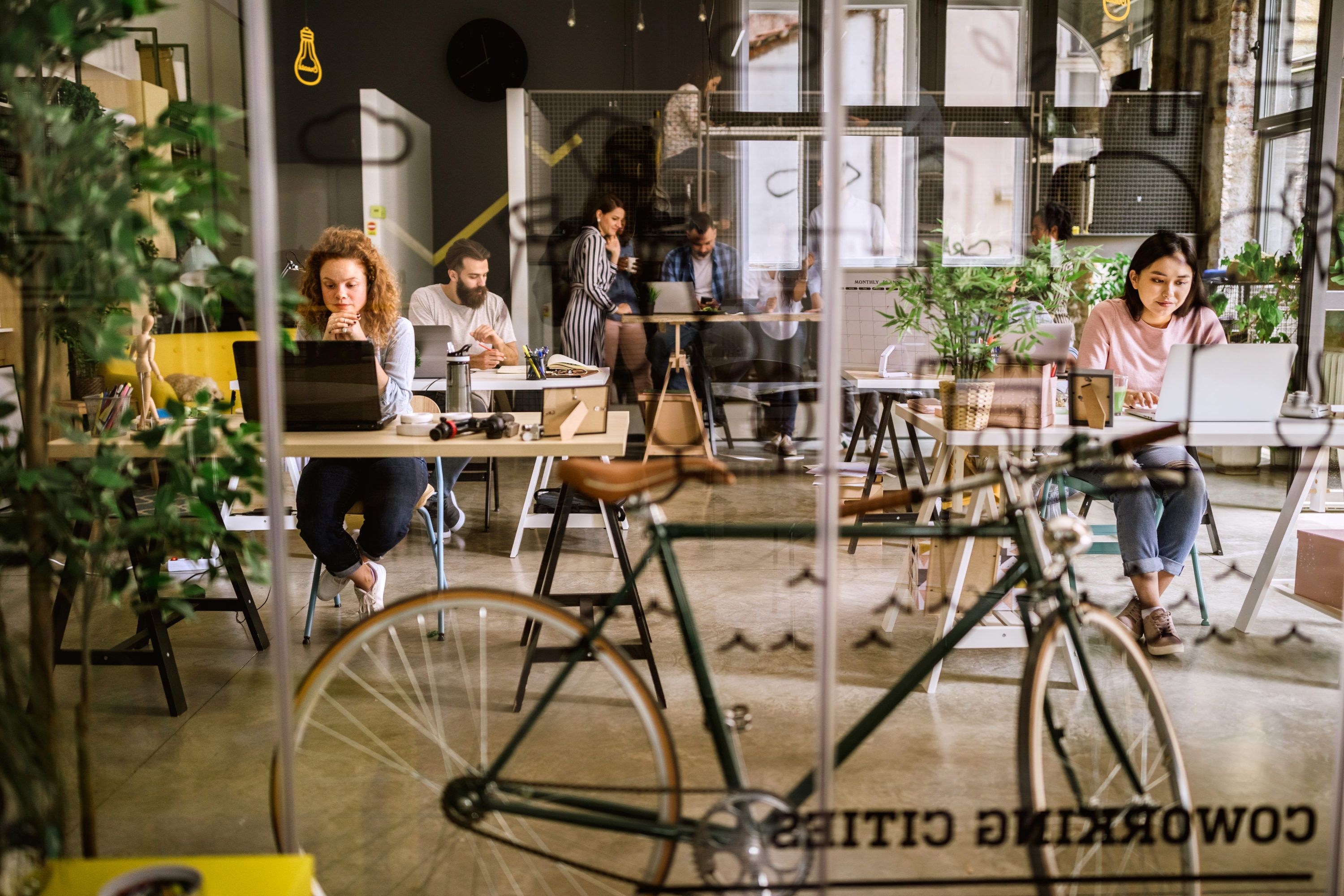  Coworking-Büro mit Fahrrad, in denen verschiedene Menschen an Schreibtischen arbeiten.