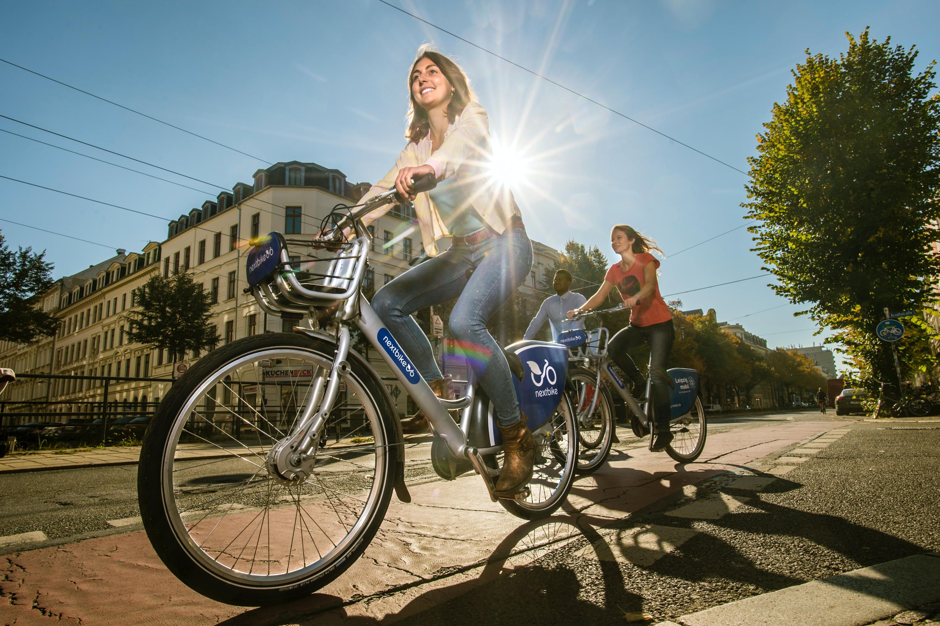 Header Bild Kategorie Mobil im Quartier: Zwei Frauen auf Fahrrädern vor sonniger Straßenkulisse.