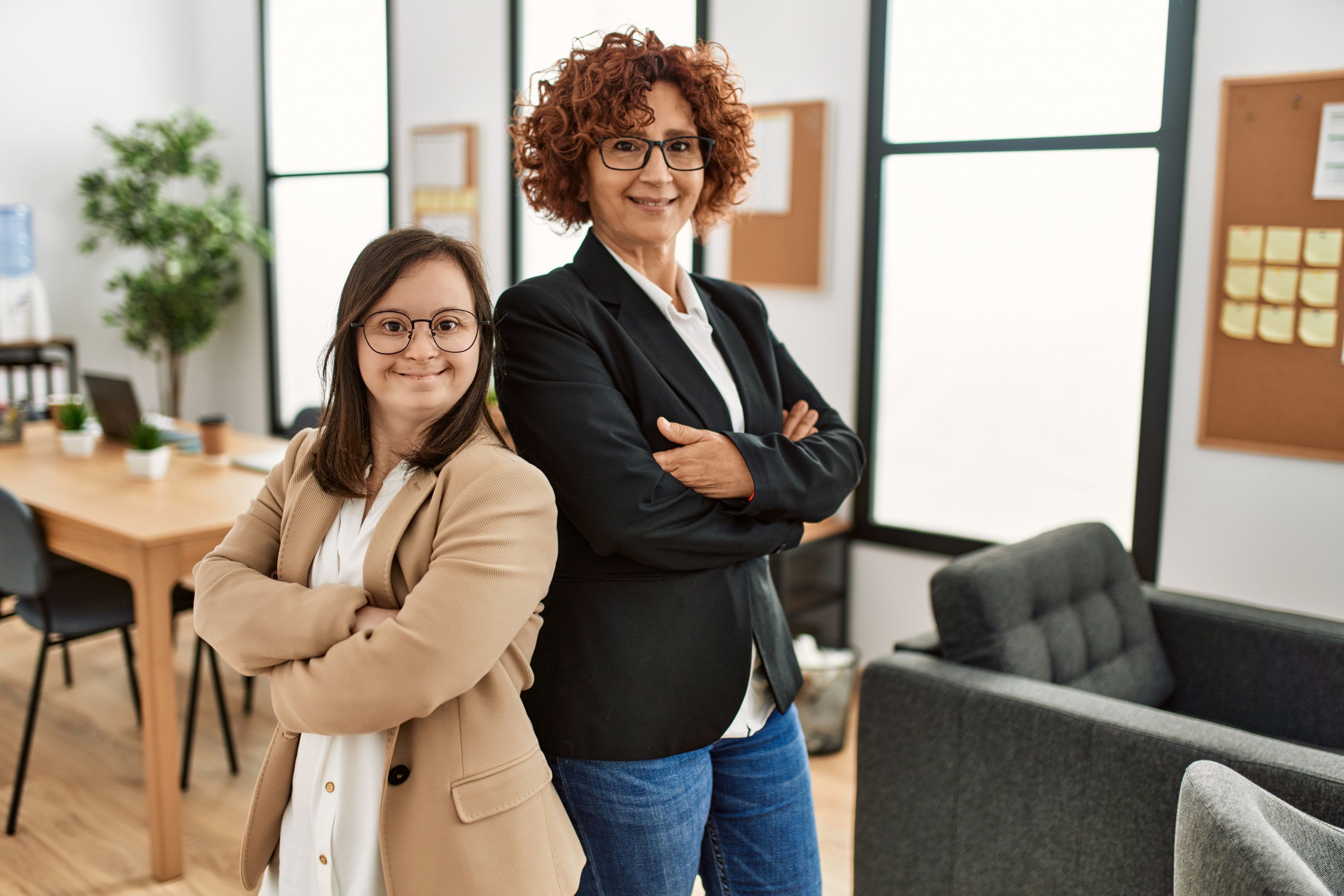 Arbeiten inklusiv mit zwei Geschäftsfrauen, davon eine mit Downsyndrom und eine ältere, stehen Rücken an Rücken 